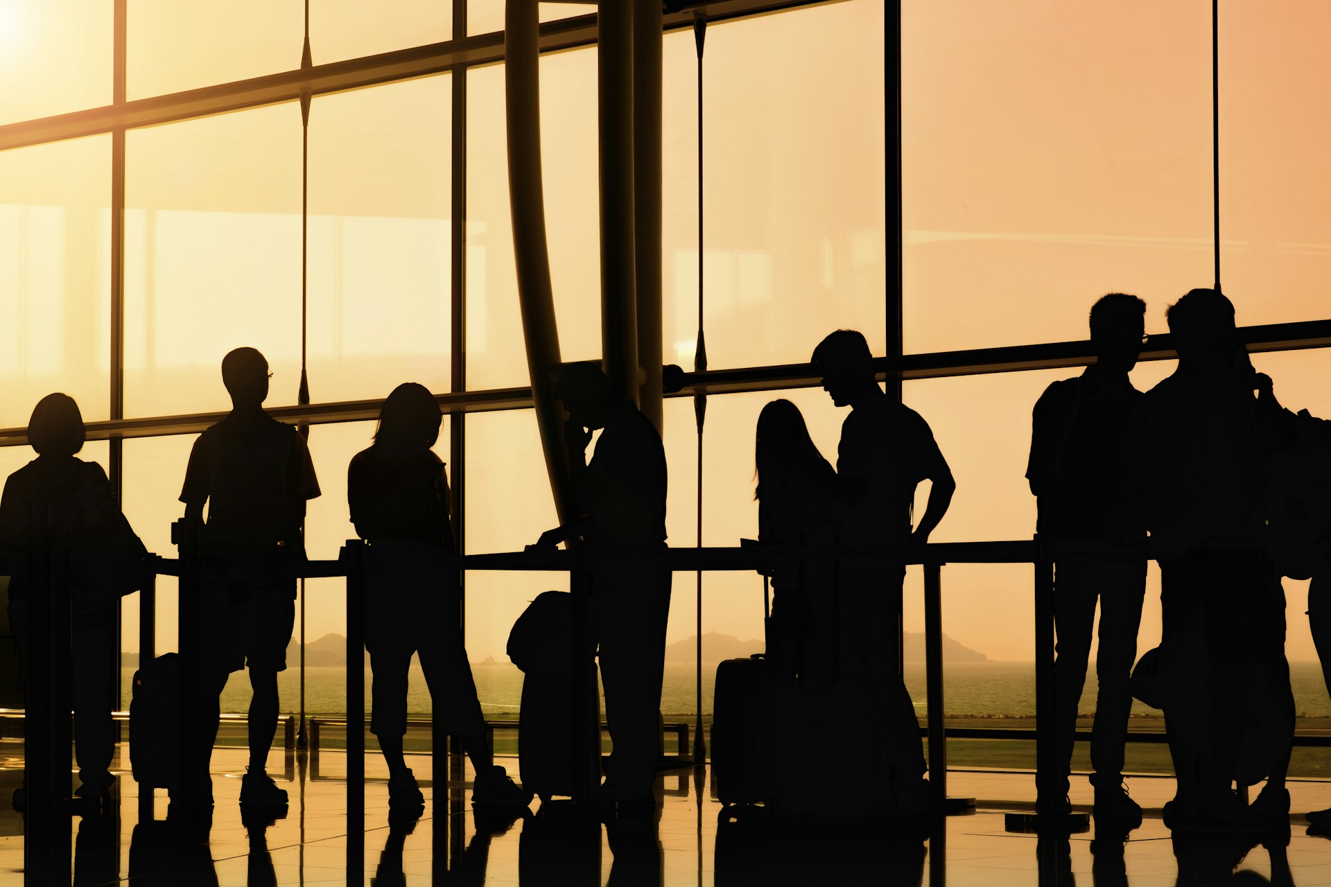 Silhouettes of passengers standing in line at an airport check-in counter