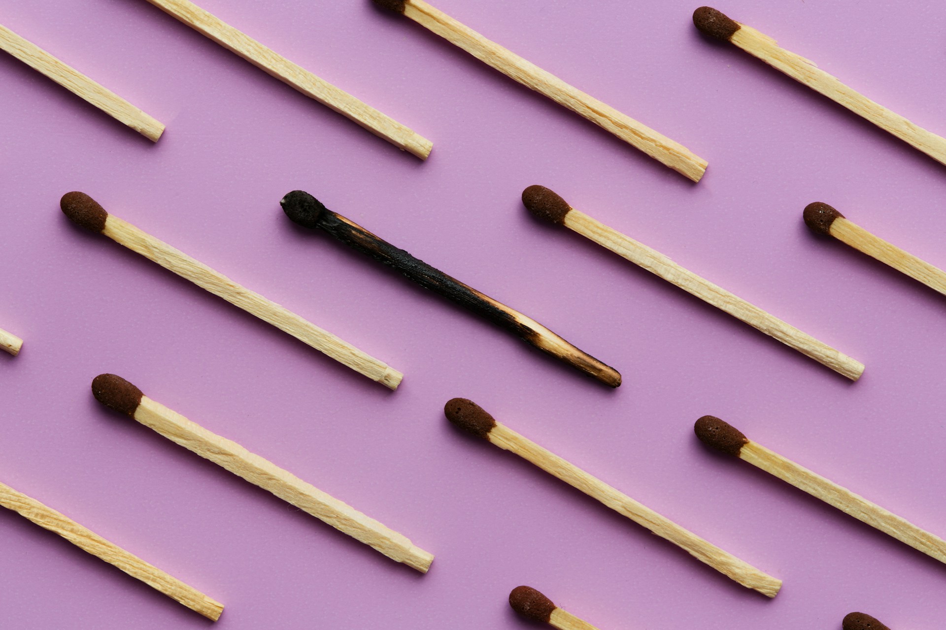 One burnt match placed among a pattern of unlit matches on a dark surface
