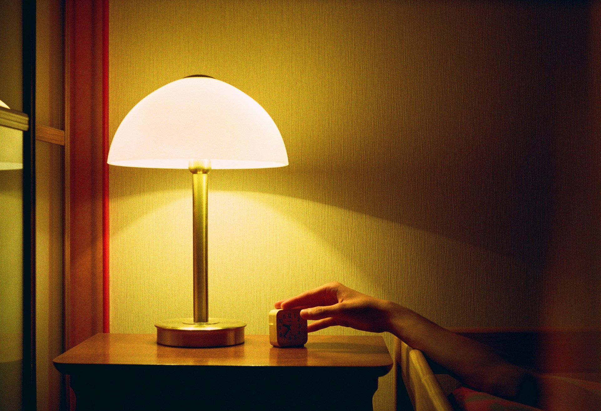 Hand resting on a table beside a lit lamp in a dim room, reflecting changes in light exposure and daily timing