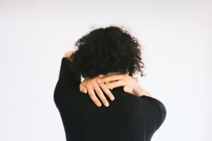 Person holding the back of their neck in natural light, representing muscle tension associated with head pain