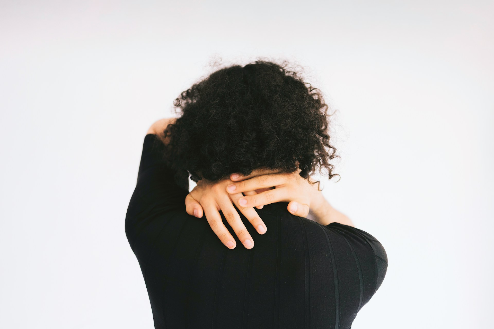 Person holding the back of their neck in natural light, representing muscle tension associated with head pain