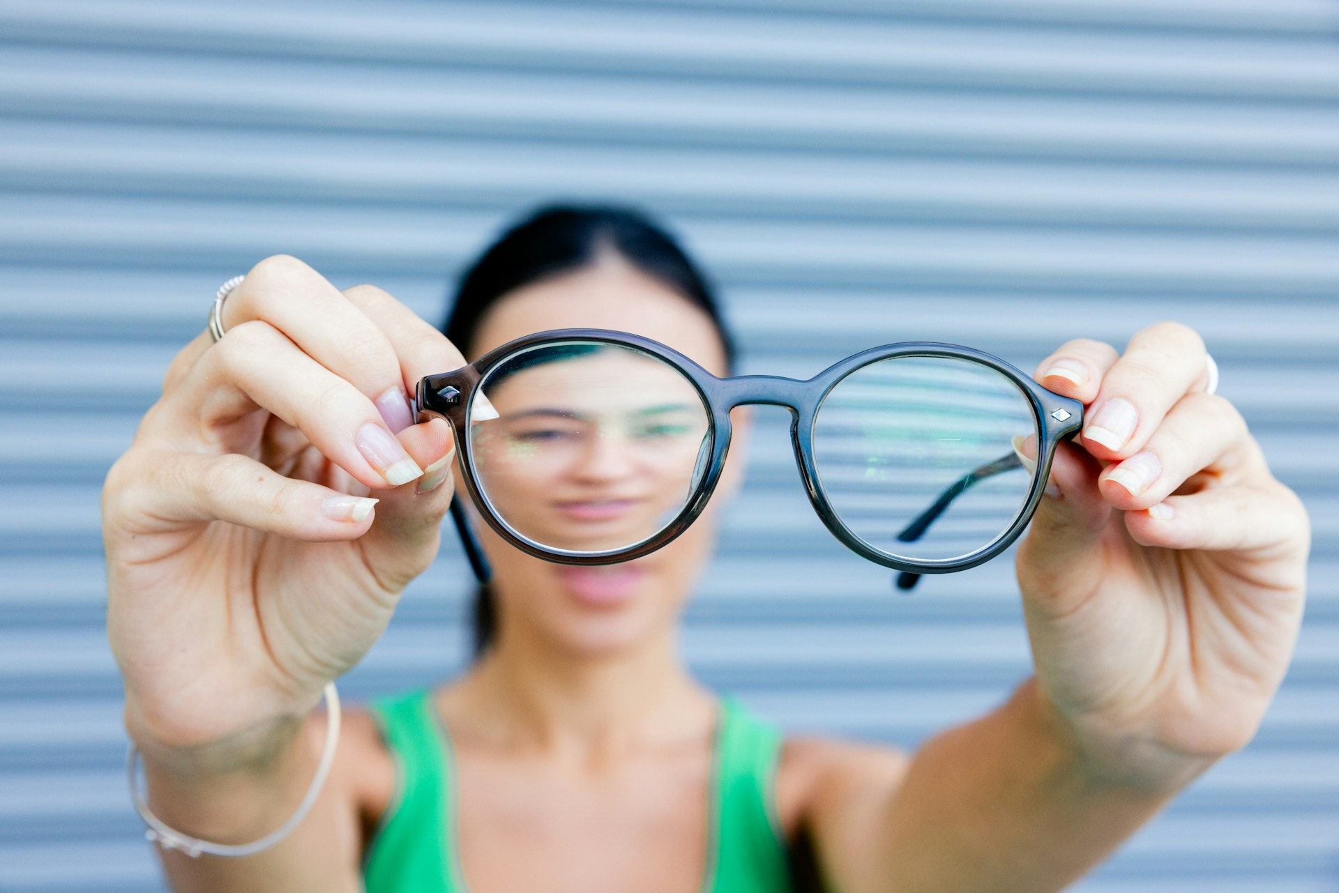 Close-up of a person holding a pair of eyeglasses against a neutral background