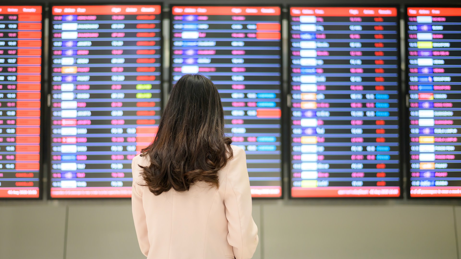 Passenger standing in an airport terminal looking at an arrivals and departures board