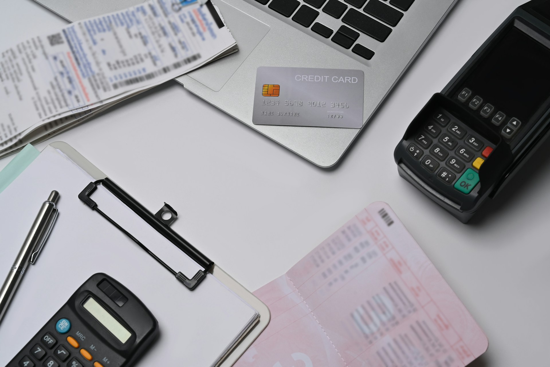 Overhead view of a laptop, calculator, bank card, and printed bills on a white desk.