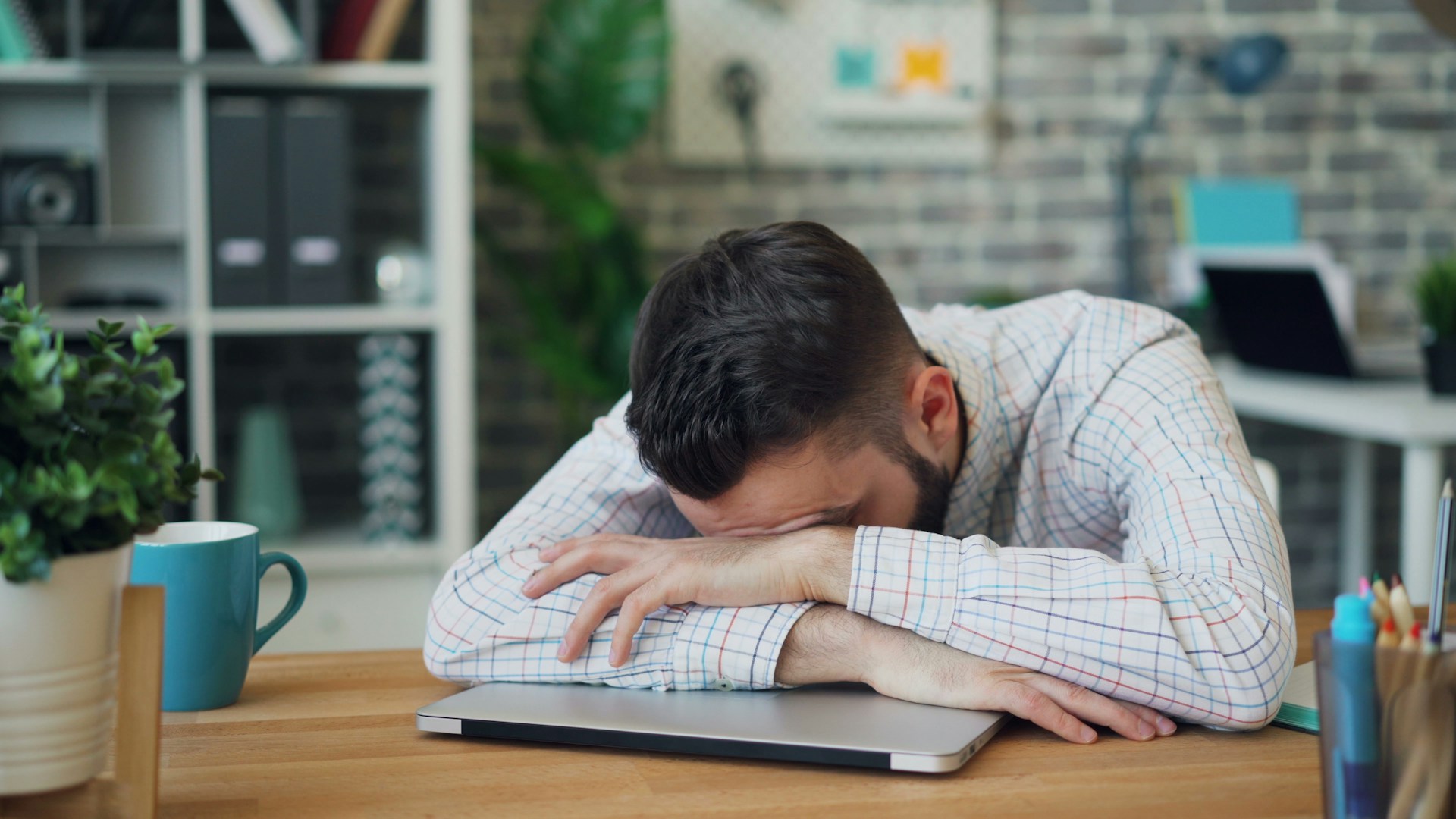 Person sitting at a desk with head in hands, appearing fatigued or low in energy