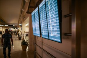 Airport departure board showing canceled flight status with traveler walking nearby