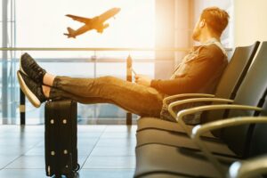 Man sitting in an airport with luggage, looking at airplanes outside the window after missing a flight