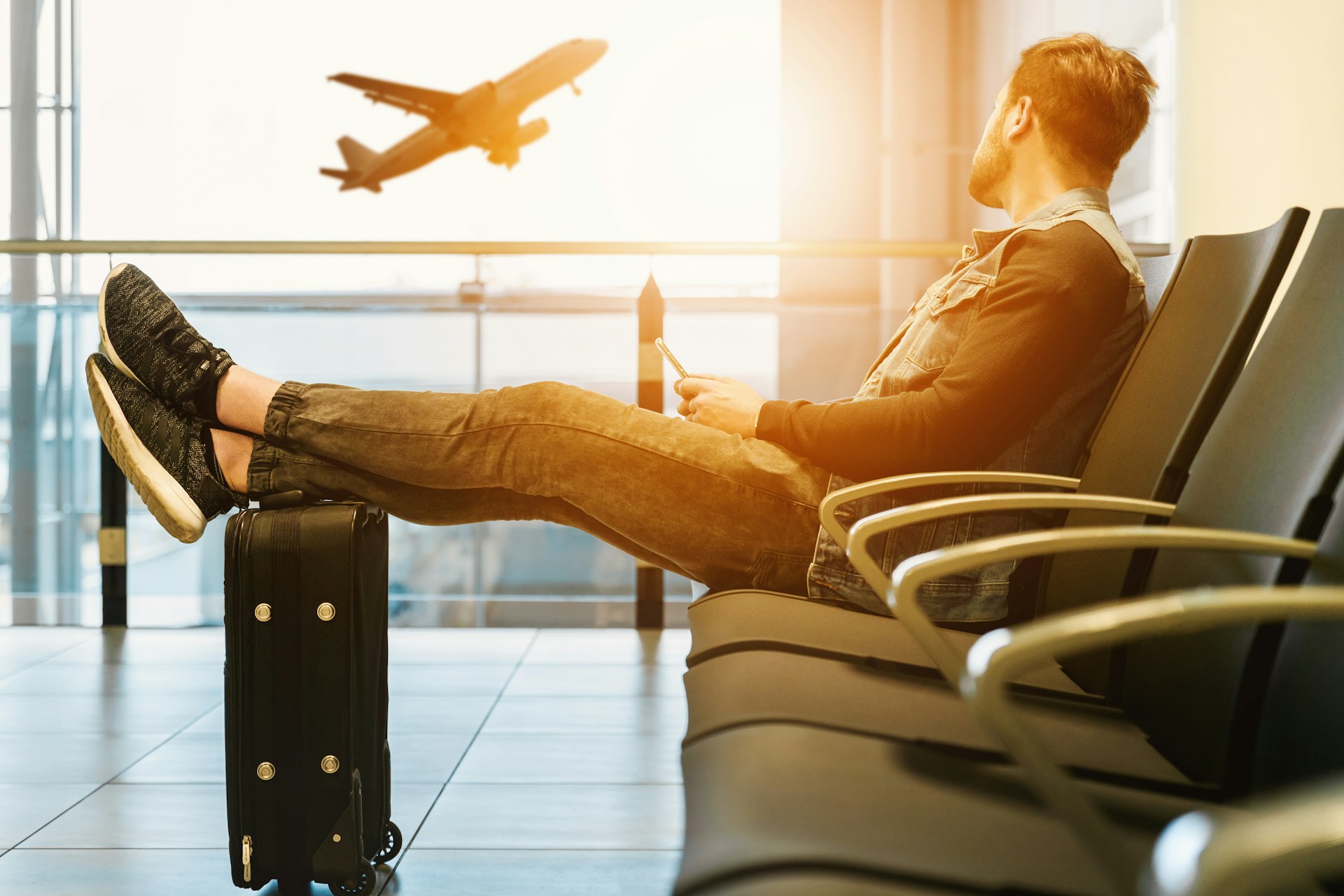 Man sitting in an airport with luggage, looking at airplanes outside the window after missing a flight