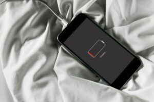 Smartphone connected to charger on white bedsheets; screen shows a battery icon and 'Charging' text.