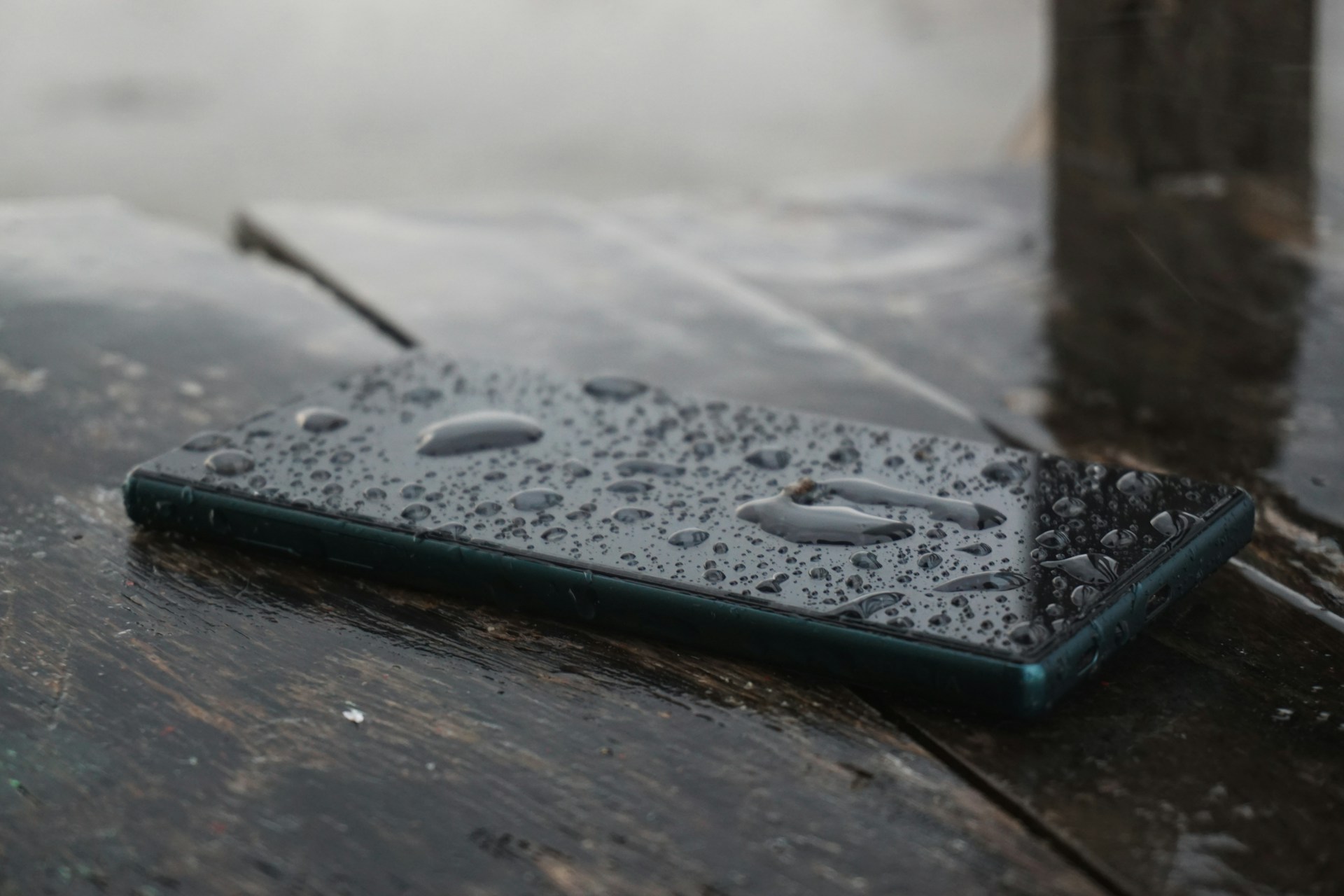 Smartphone resting on a wooden surface with water droplets visible on the screen.