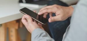 Person holding a smartphone with the screen turned off while seated indoors.