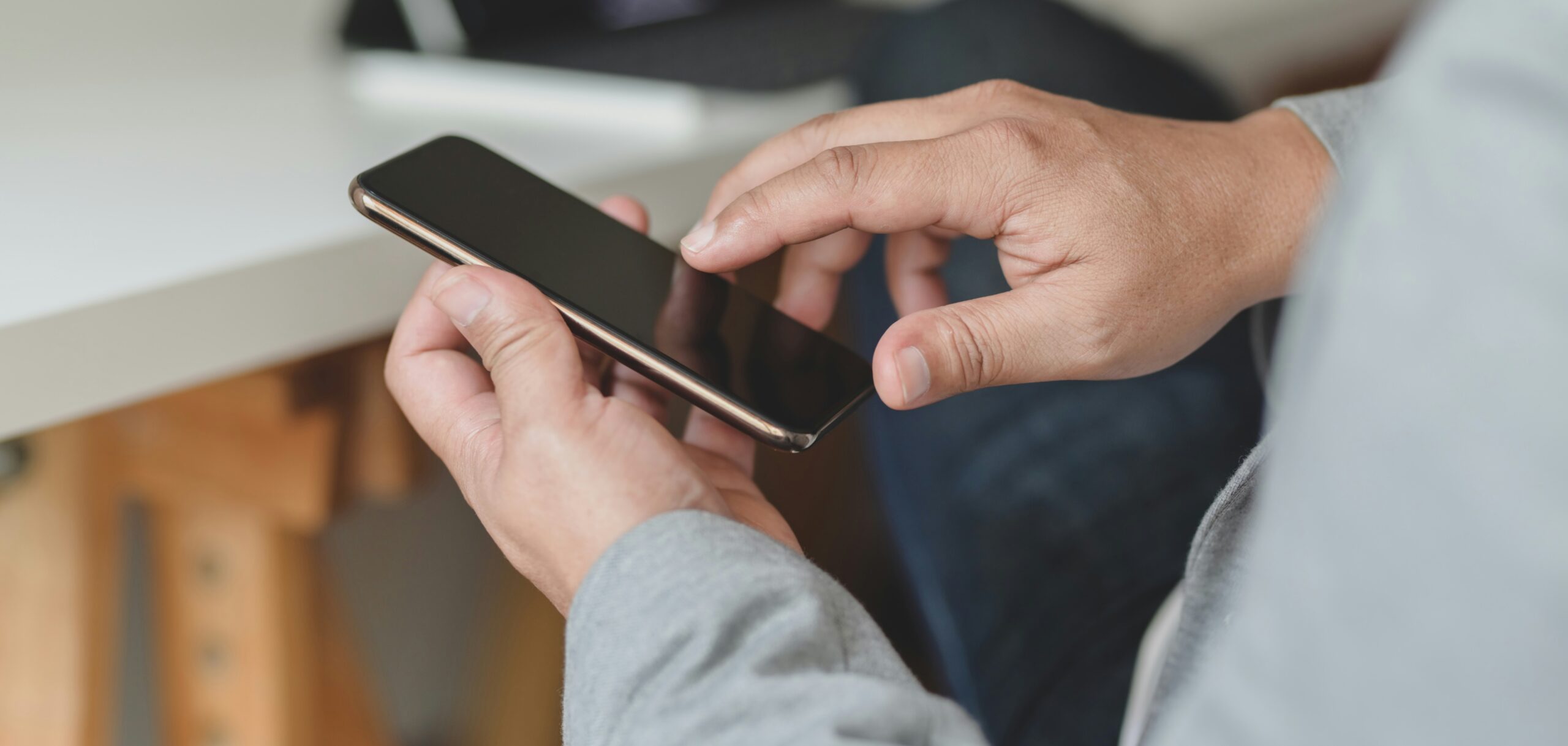 Person holding a smartphone with the screen turned off while seated indoors.