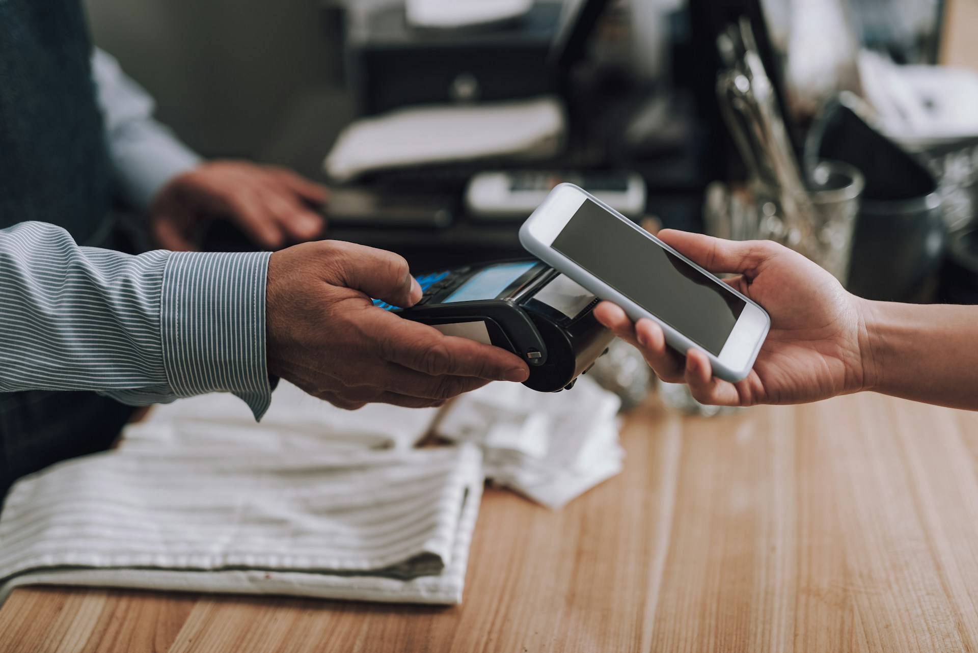 Customer making a contactless payment at a checkout terminal while a store employee operates the register