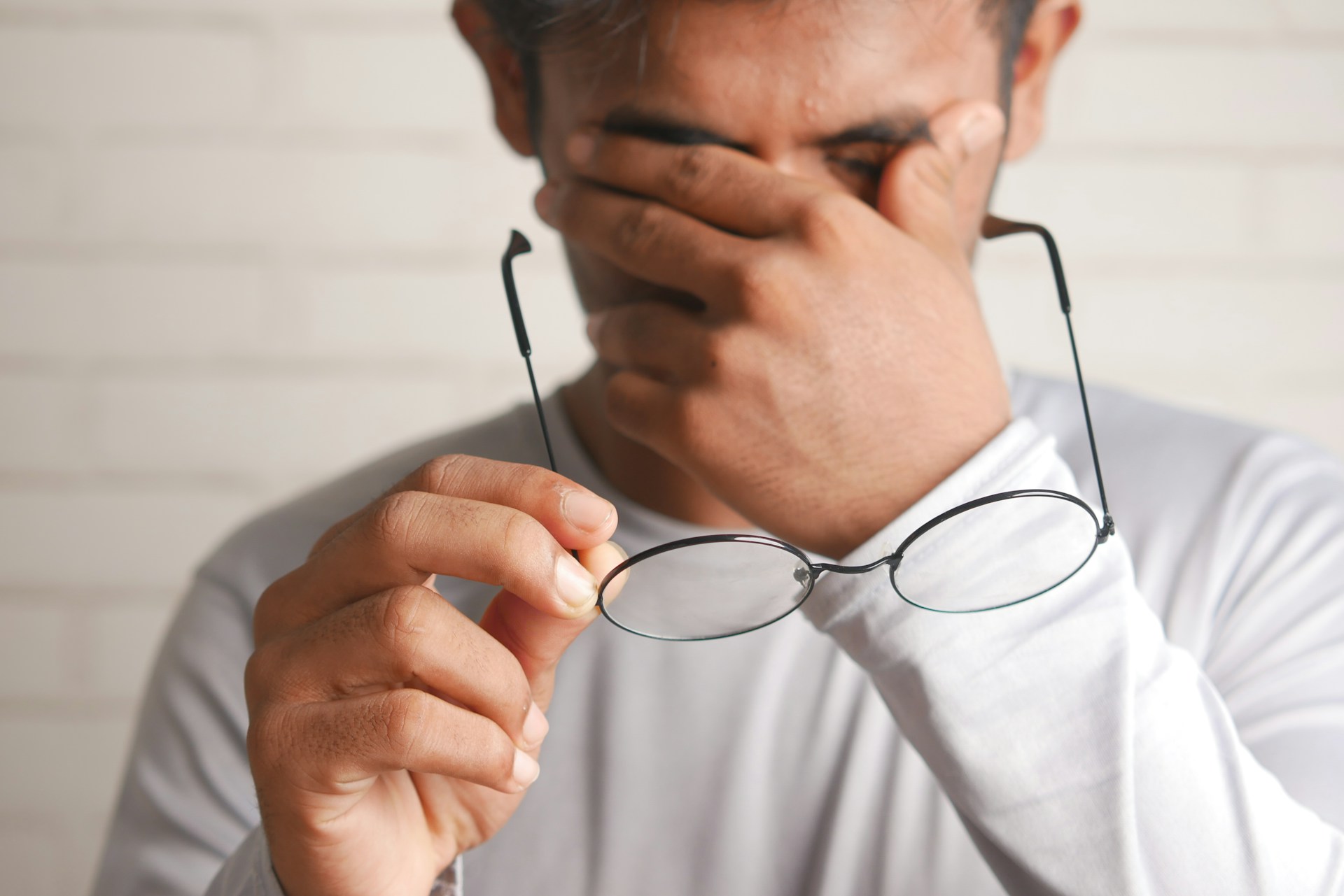 Person holding eyeglasses near their face, illustrating eye fatigue and blinking associated with tiredness.