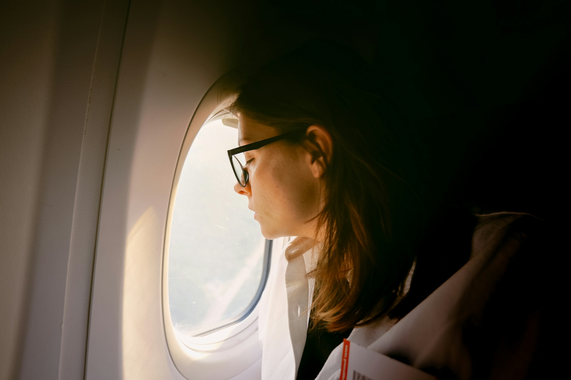 Passenger looking out an airplane window during a flight, when changes in air pressure can cause ears to pop.