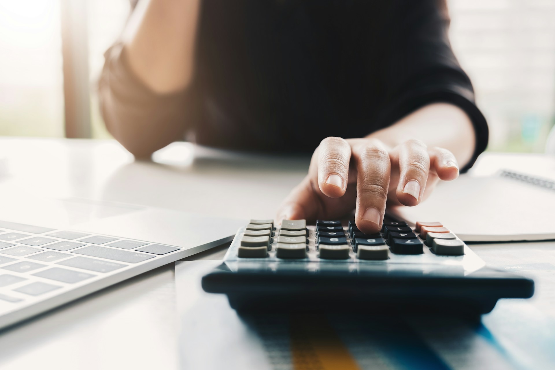 Person using a calculator and laptop while reviewing bank account finances