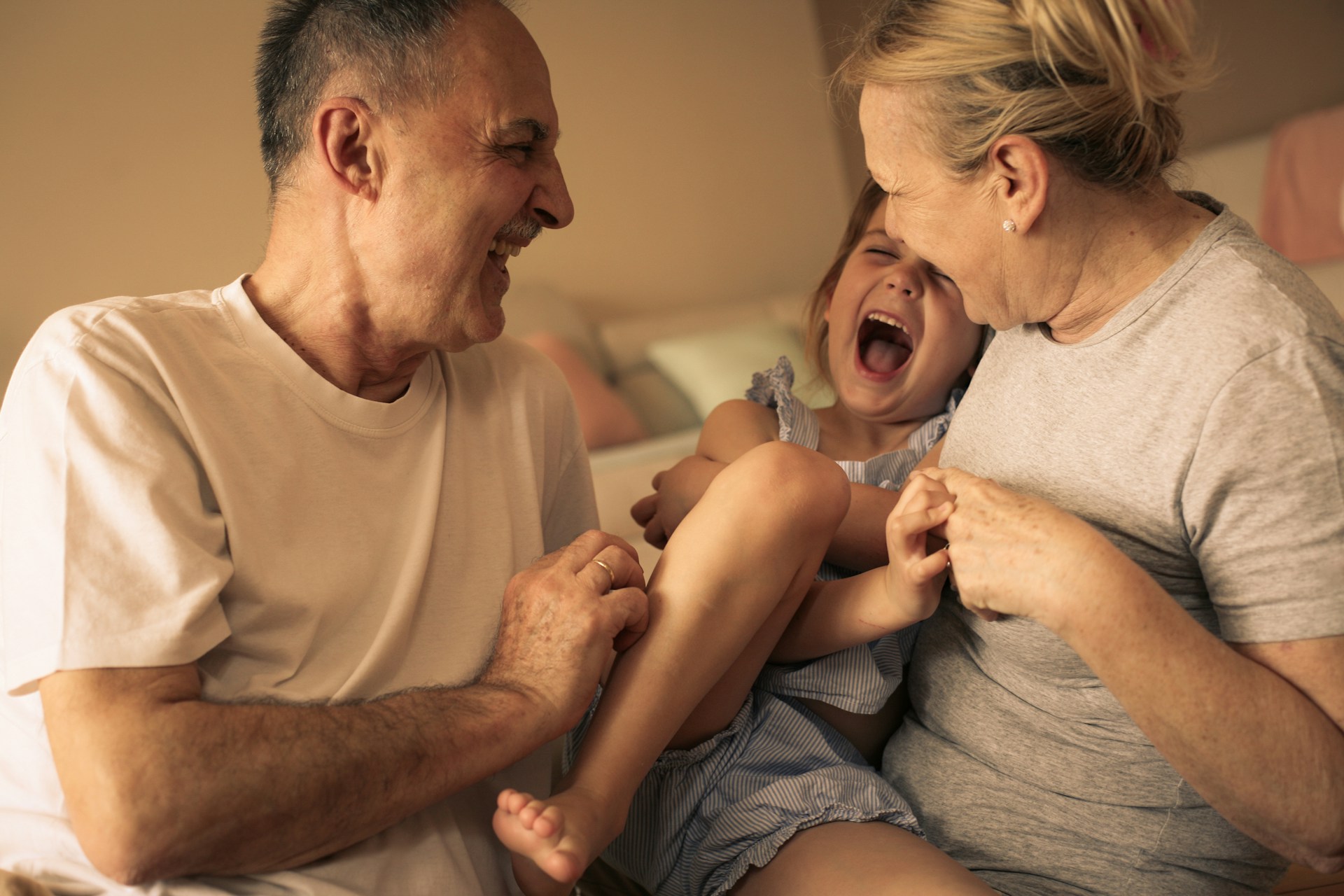 Grandparents playing with their granddaughter during a playful moment that shows a natural reaction to touch and interaction.
