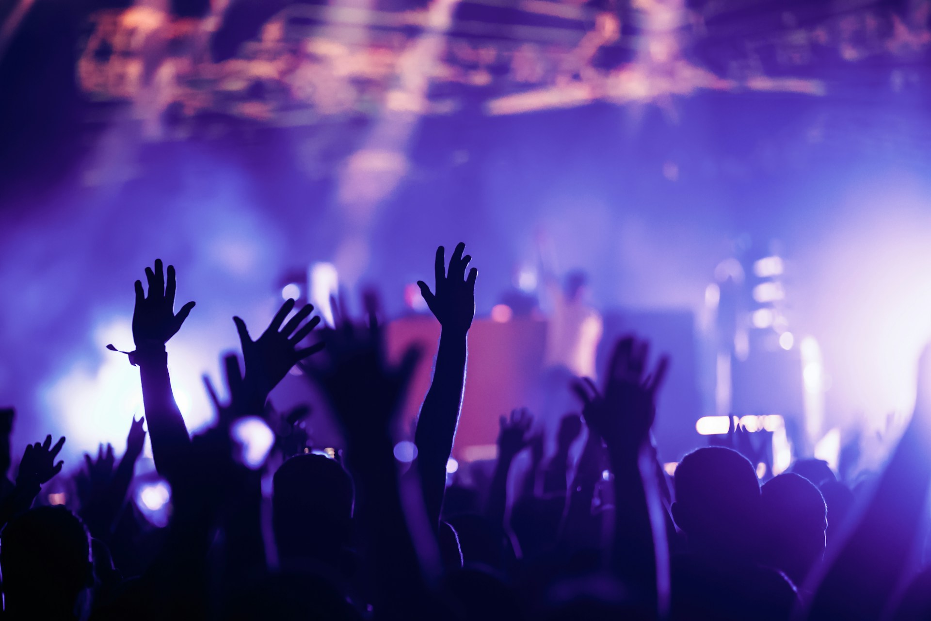 Crowd at an outdoor concert with raised hands during a loud live music performance.