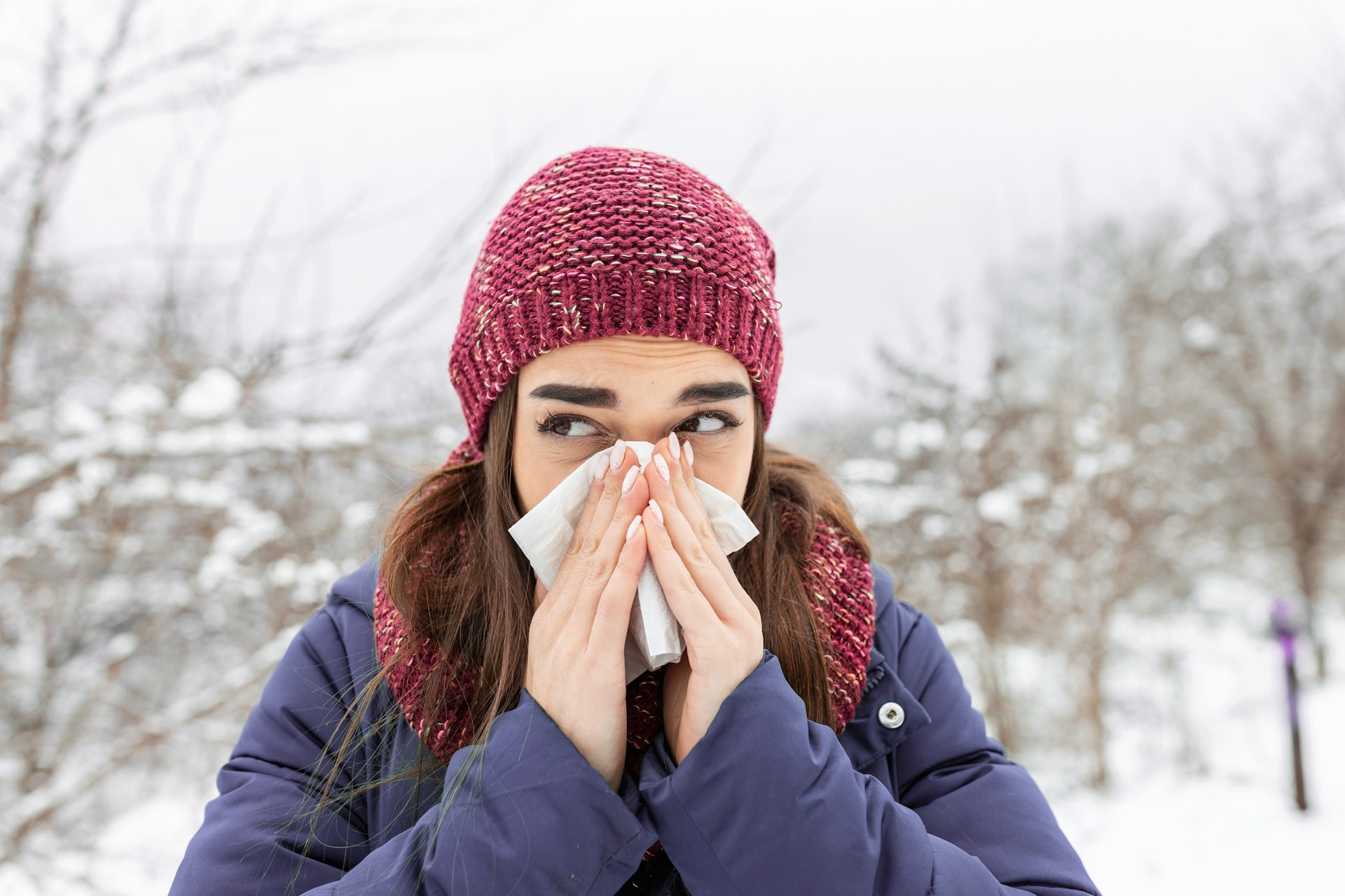 Person outdoors in cold weather using a tissue while experiencing a runny nose