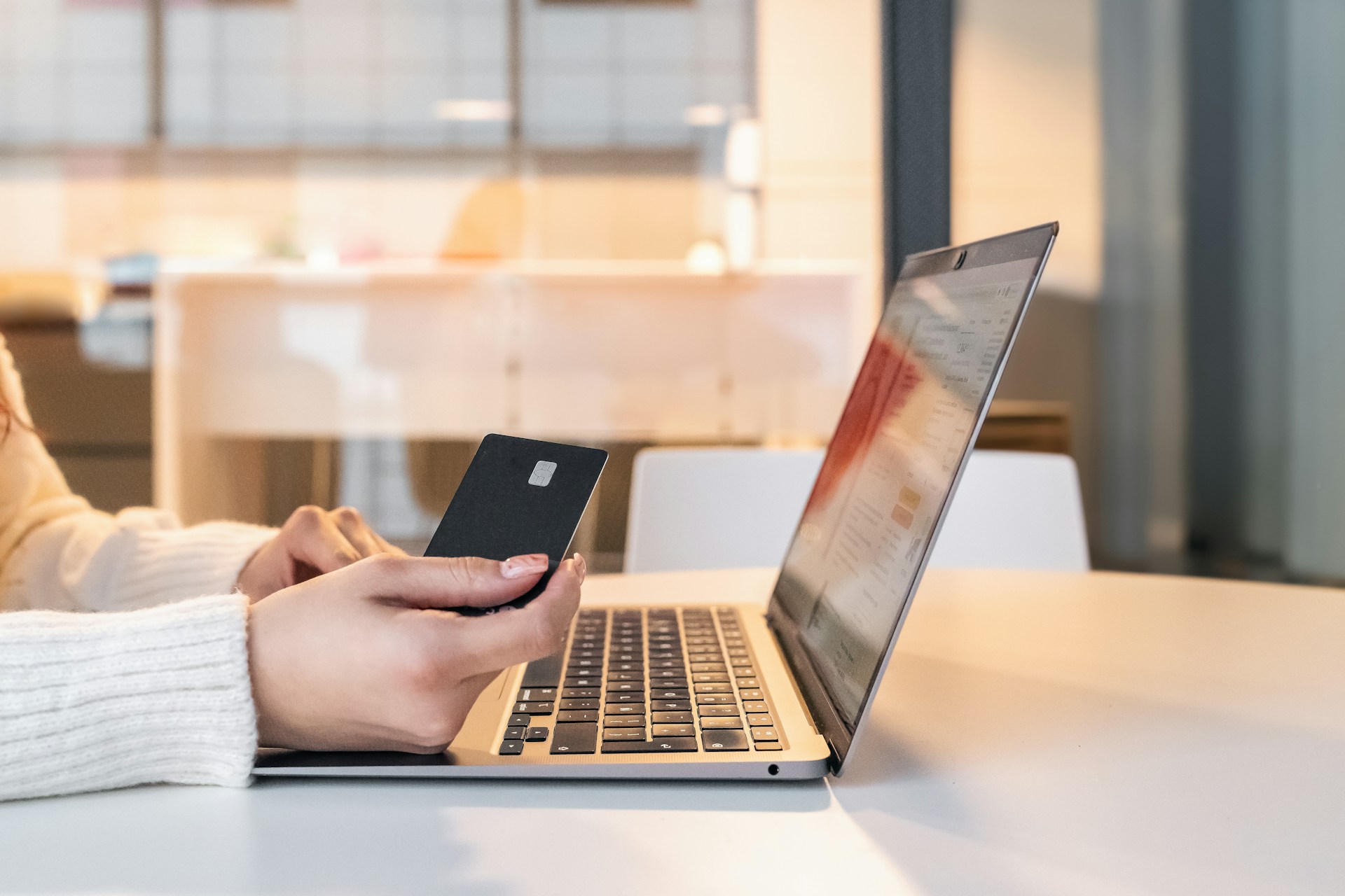 Person holding a smartphone while viewing financial information on a laptop.