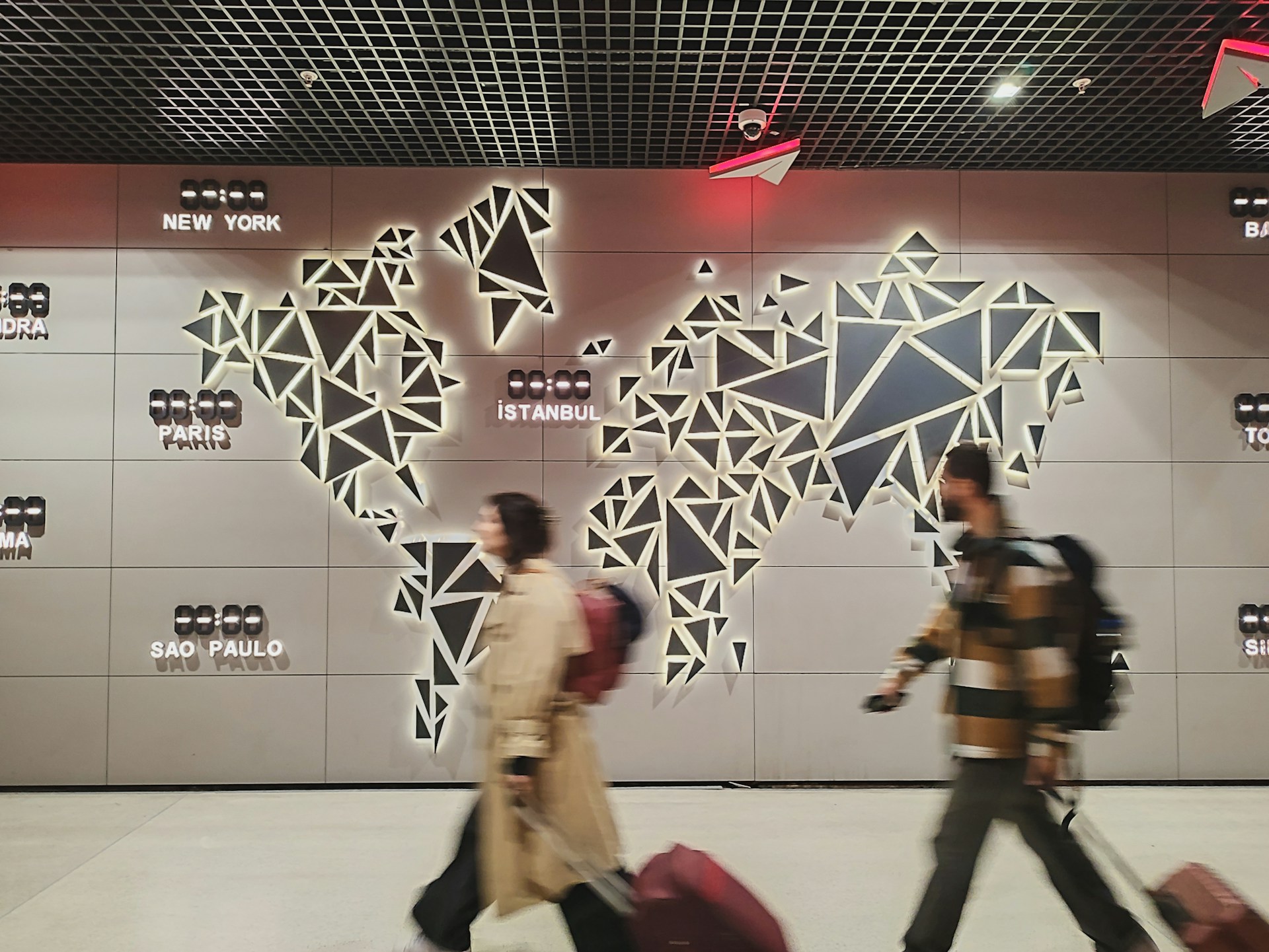 Travelers walking past a large world map display inside an international airport terminal.
