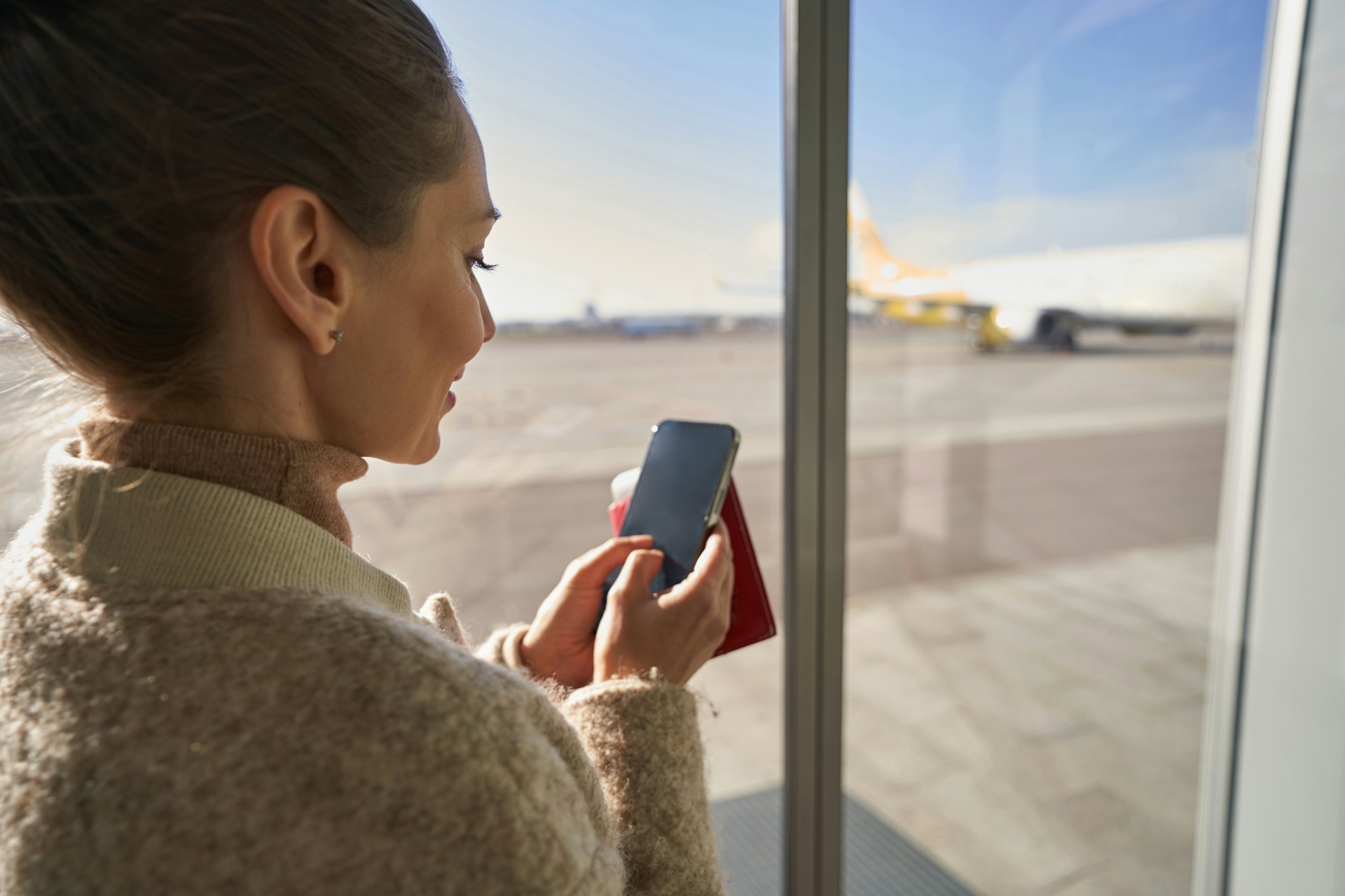 Traveler using a mobile phone while holding passport and travel documents at an airport before an international flight.