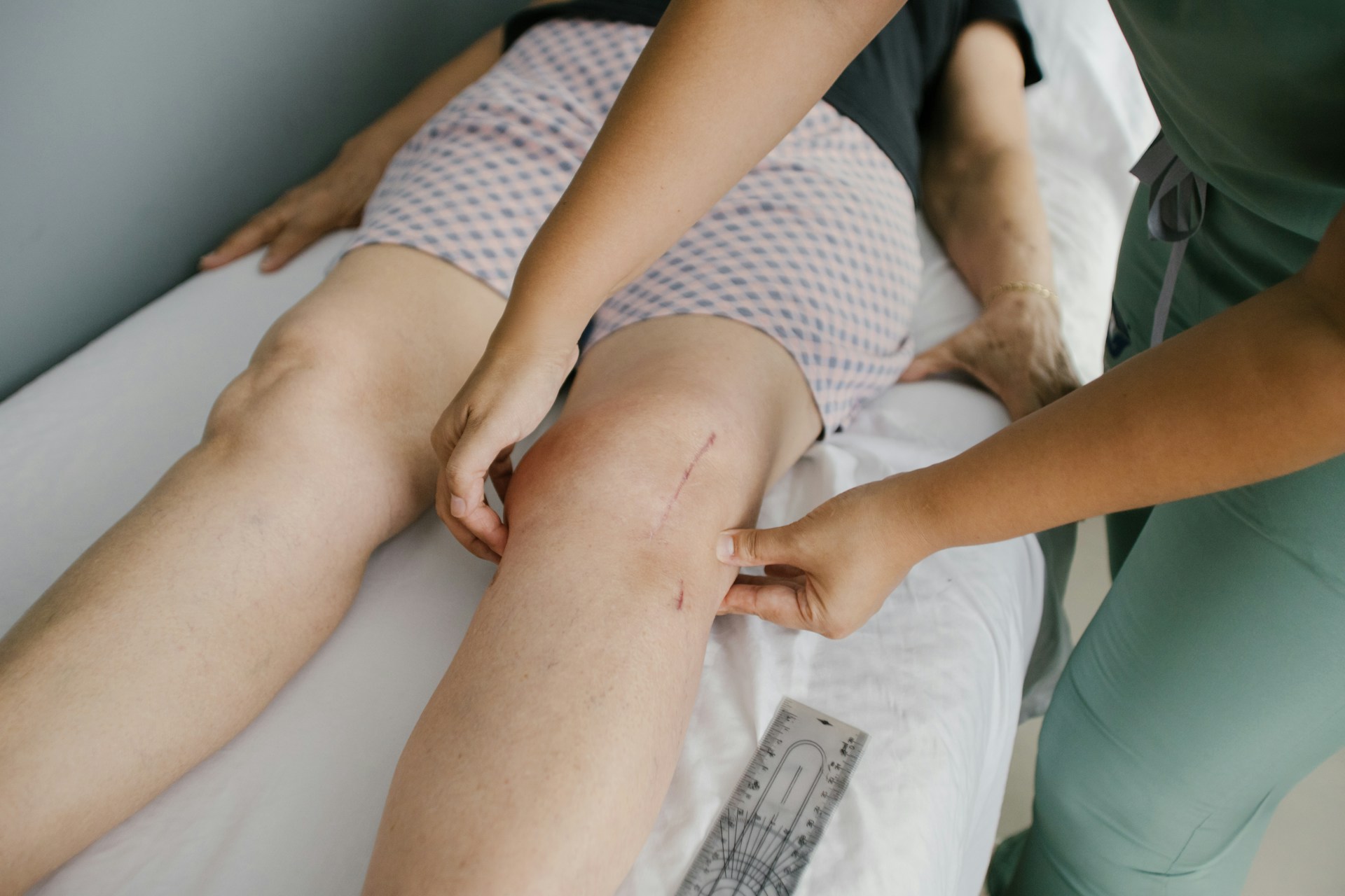 Medical professional examining a scar on a patient's knee during a skin assessment.