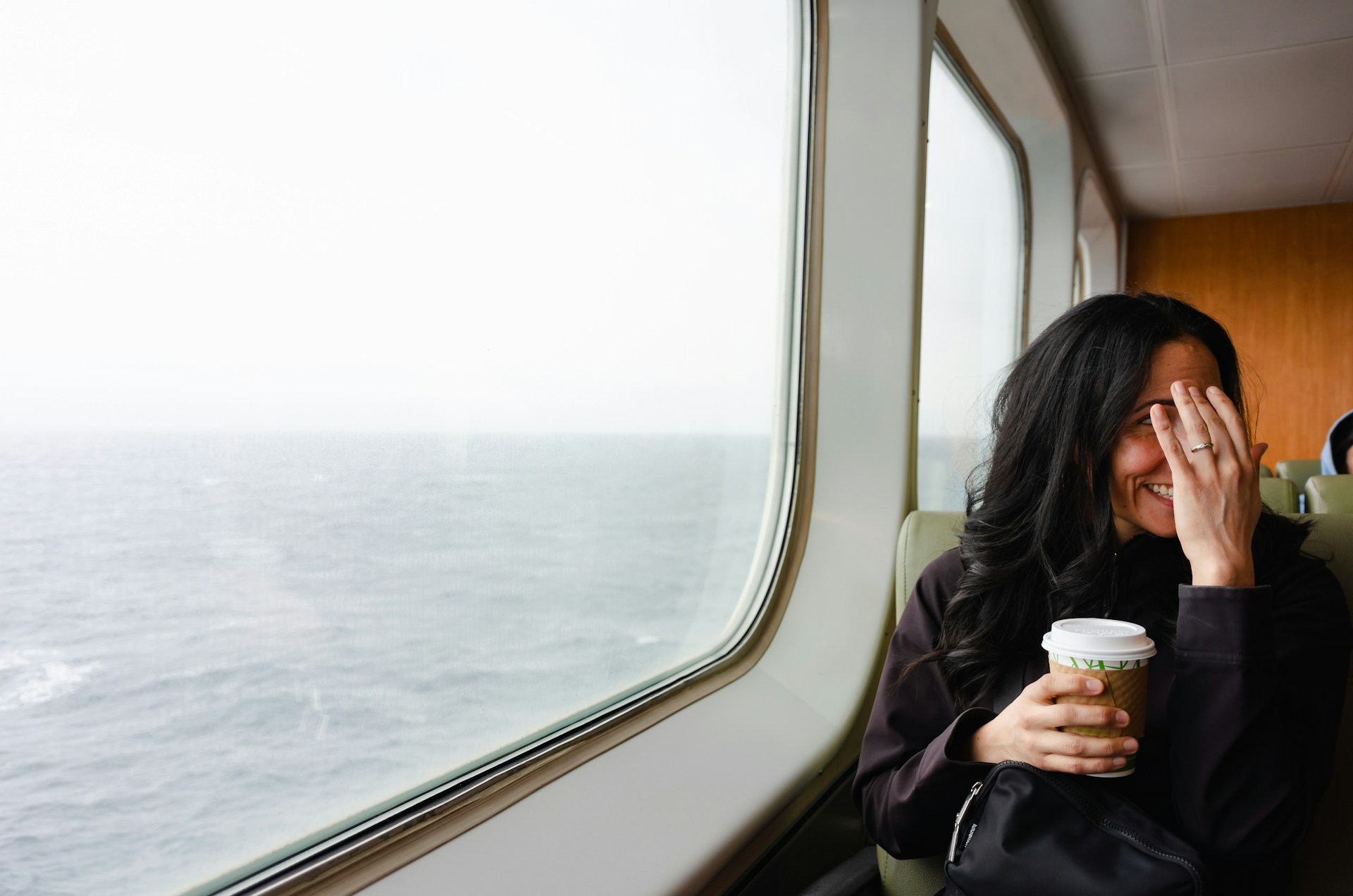 Person smiling with a hand partially covering their face while sitting on public transportation.