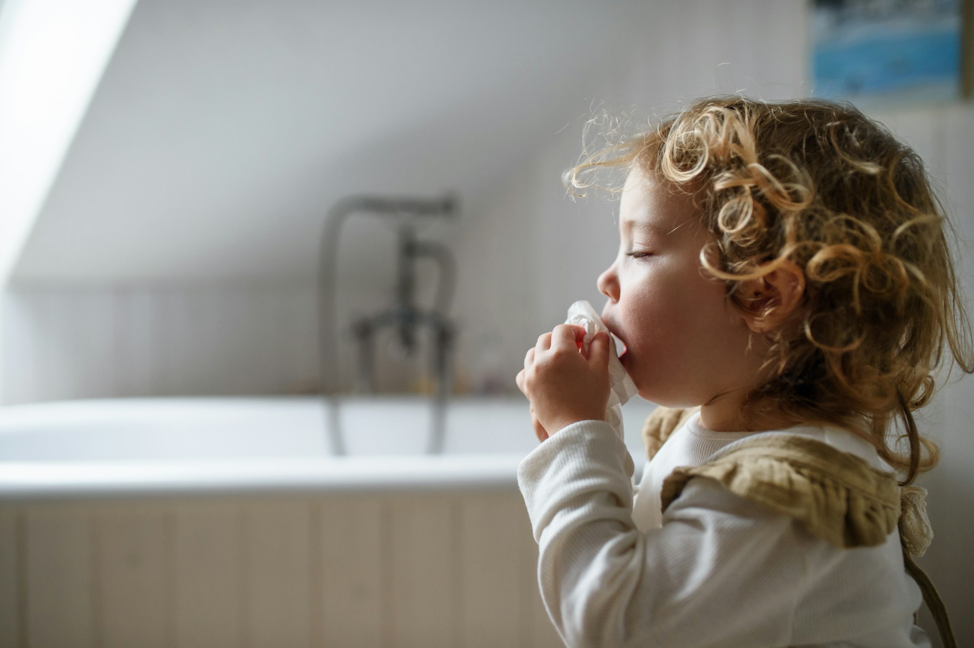 Young child sneezing while sitting on the floor indoors, illustrating the body's natural sneeze reflex.