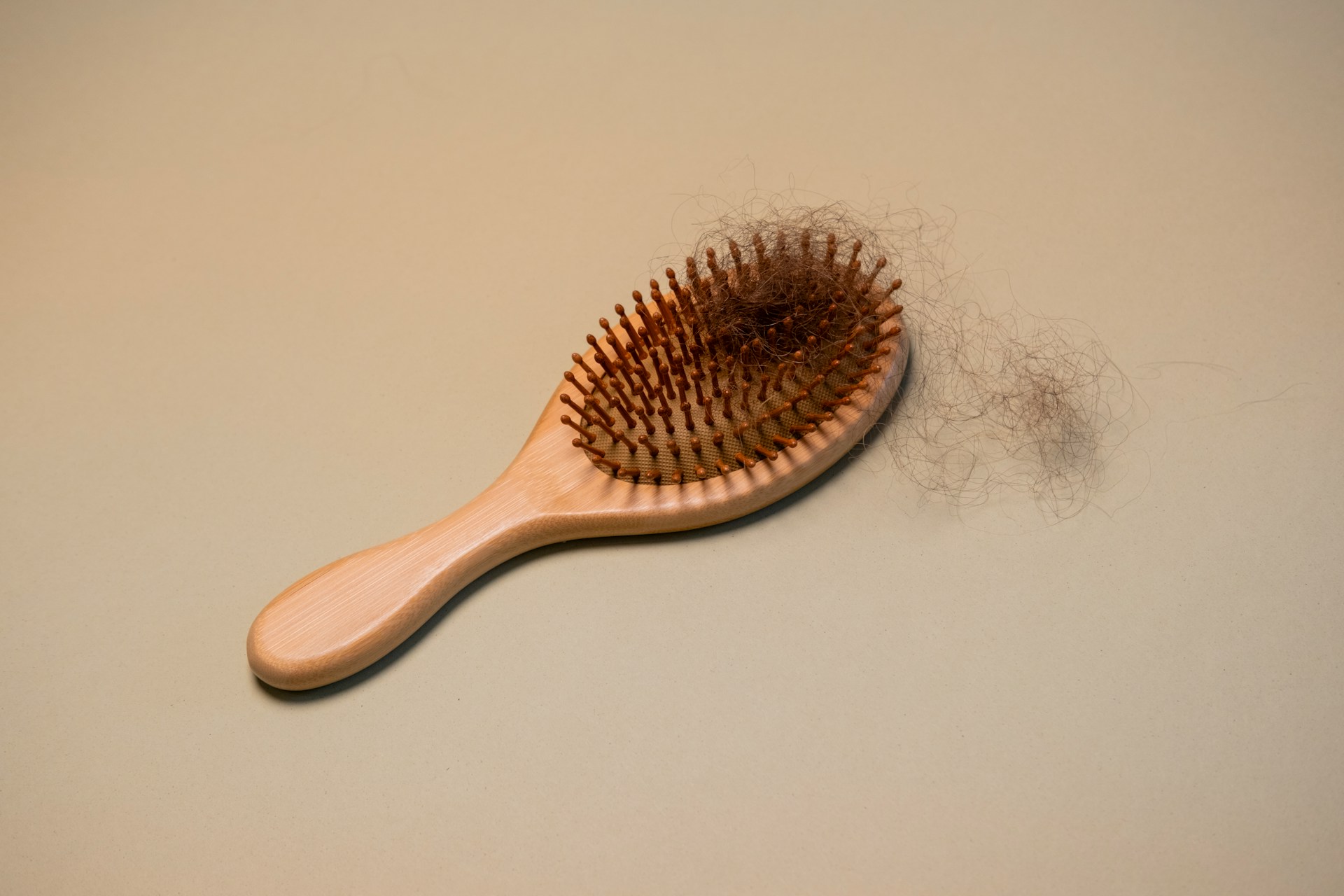 Wooden hairbrush with naturally shed hair resting on a plain background.