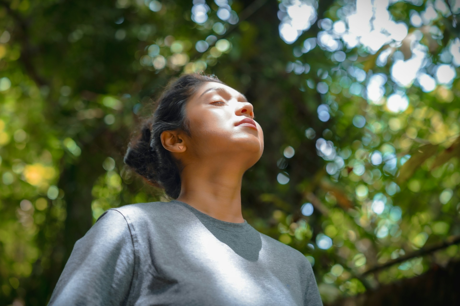 Woman standing outdoors with her eyes closed while taking a calm breath.